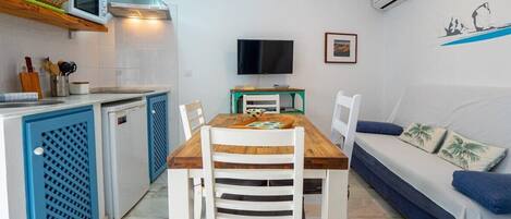 A compact kitchen with a dining area, a TV, and a sofa.
