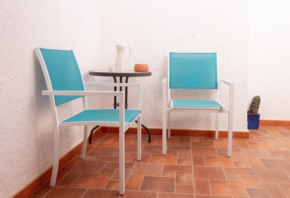 Dos sillas blancas con cojines azules y una mesita con una jofaina blanca y un cuenco de madera.