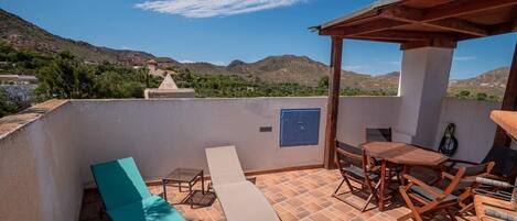 Terraza en la azotea con vistas a montañas, una mesa y sillas de madera, y dos sillones de relax.
