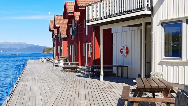 A wooden deck with outdoor seating and a lifebuoy on a building by a body of water. - 5 Person Holiday Home in Sjernaroy (Stavanger)