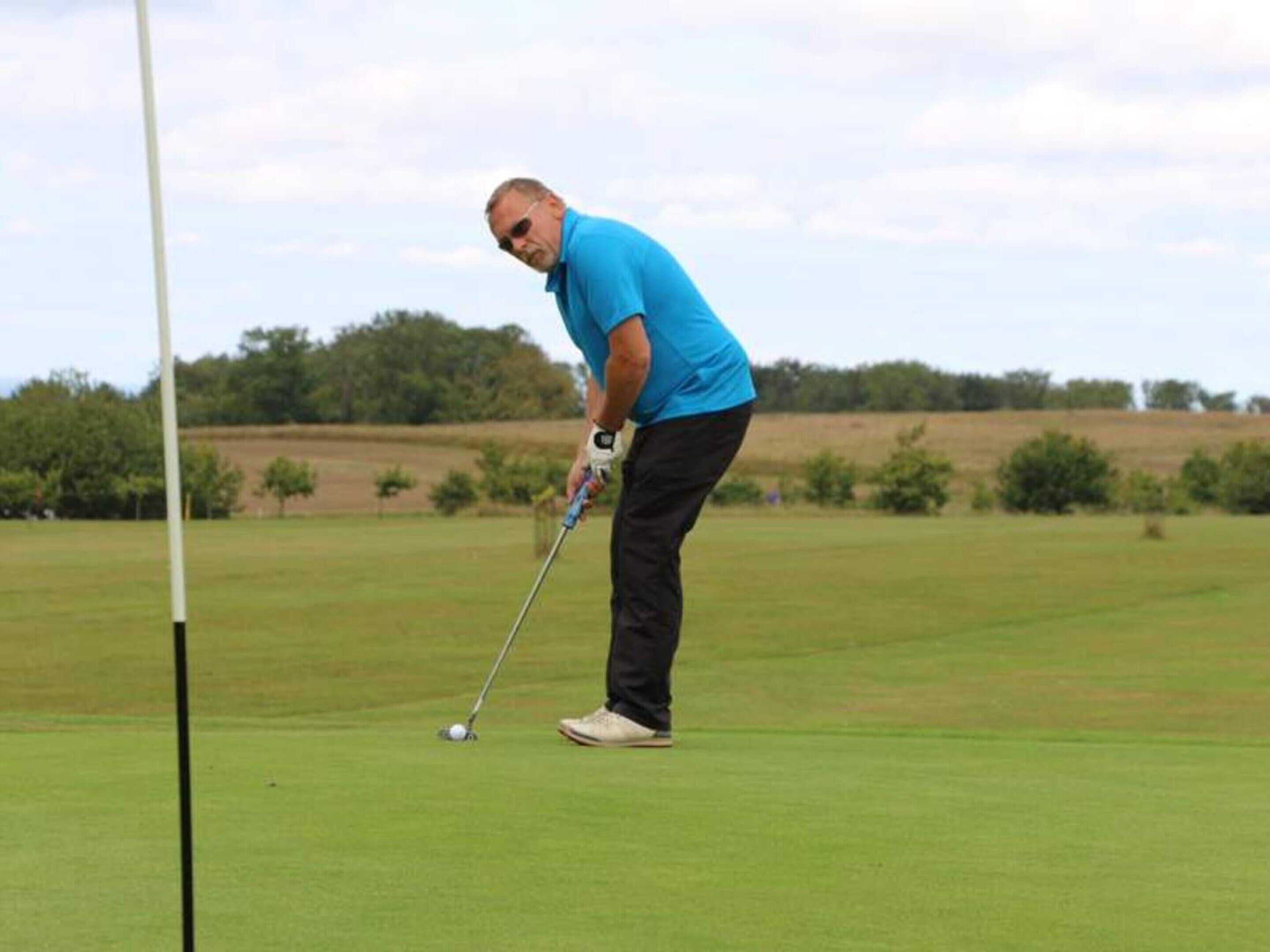 A person in a blue shirt and black pants preparing to put a golf ball on a green field.