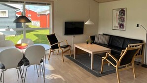 Ein modernes Wohnzimmer mit Sofa, Sesseln, Fernseher und einem Essbereich mit Tisch und Stühlen.