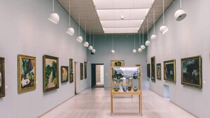 Eine Kunstgalerie mit einer zentralen Vitrine und Gemälden an den Wänden.