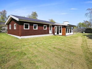 Een huis met twee verdiepingen, een schuin dak, een overdekte veranda en een omheinde tuin.