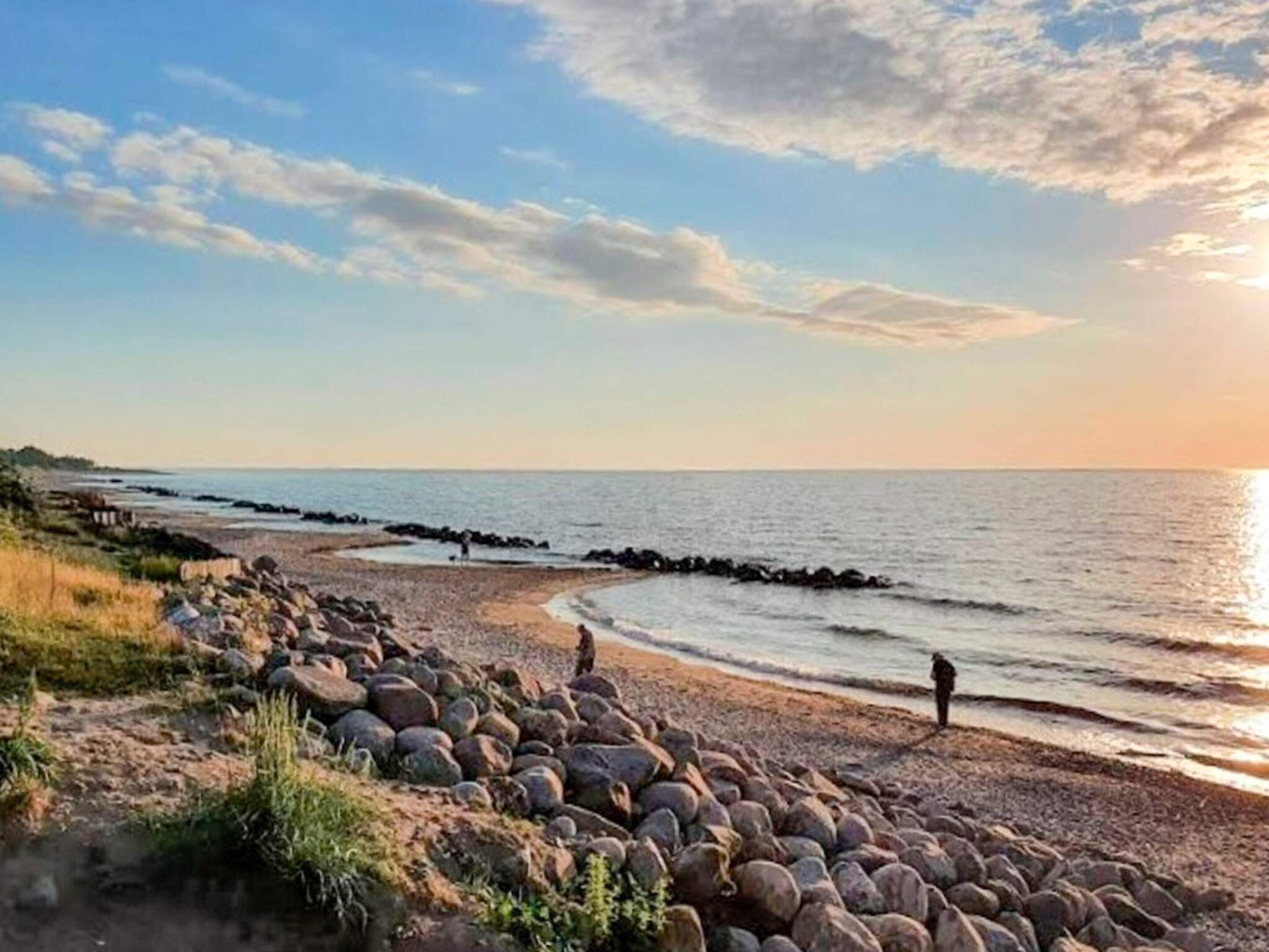 Un paisaje costero con costa rocosa, una persona de pie cerca del agua y cielo despejado.