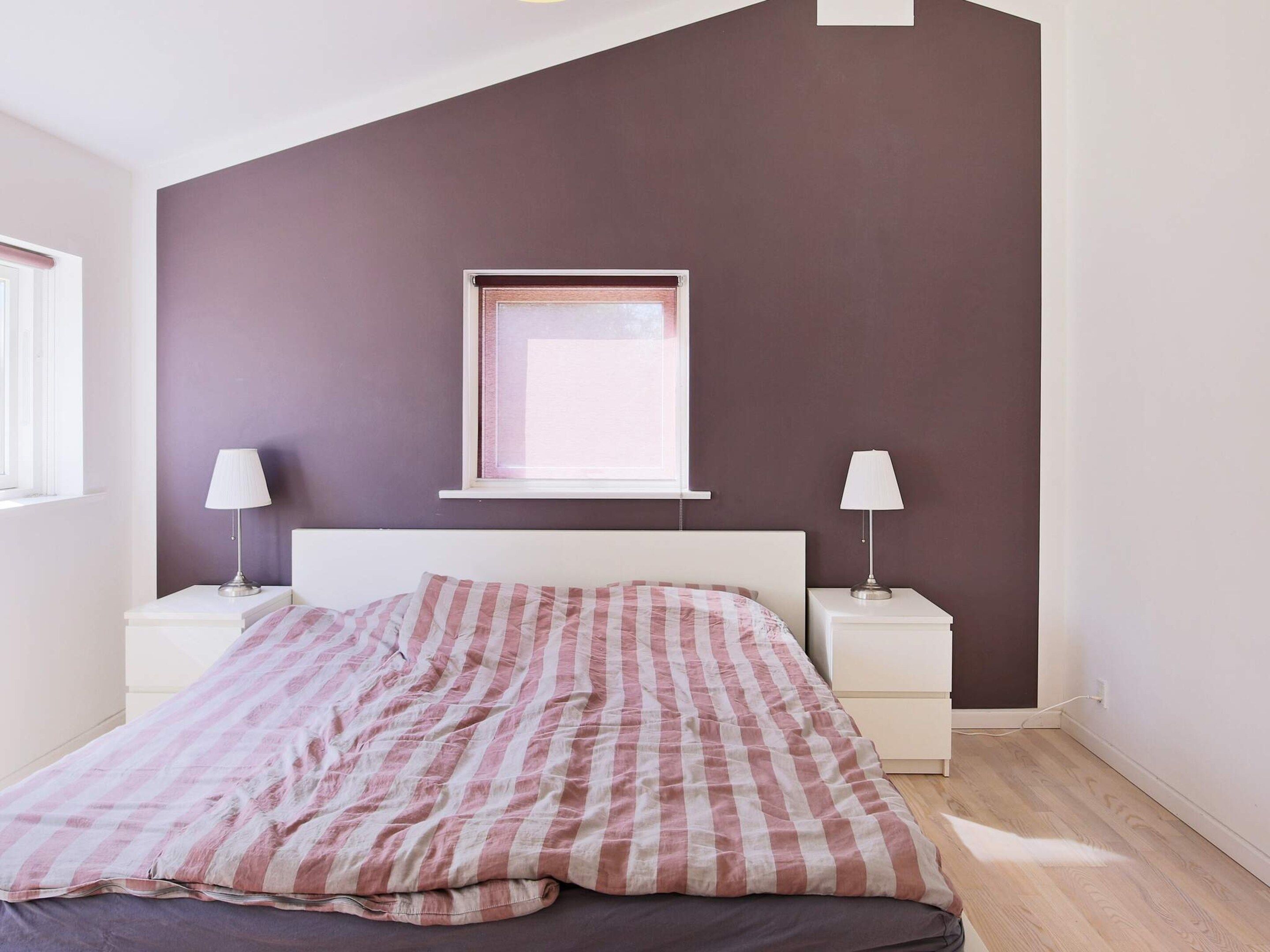 Un dormitorio con una cama, dos mesitas de noche, una ventana y un cuadro colgado en la pared.