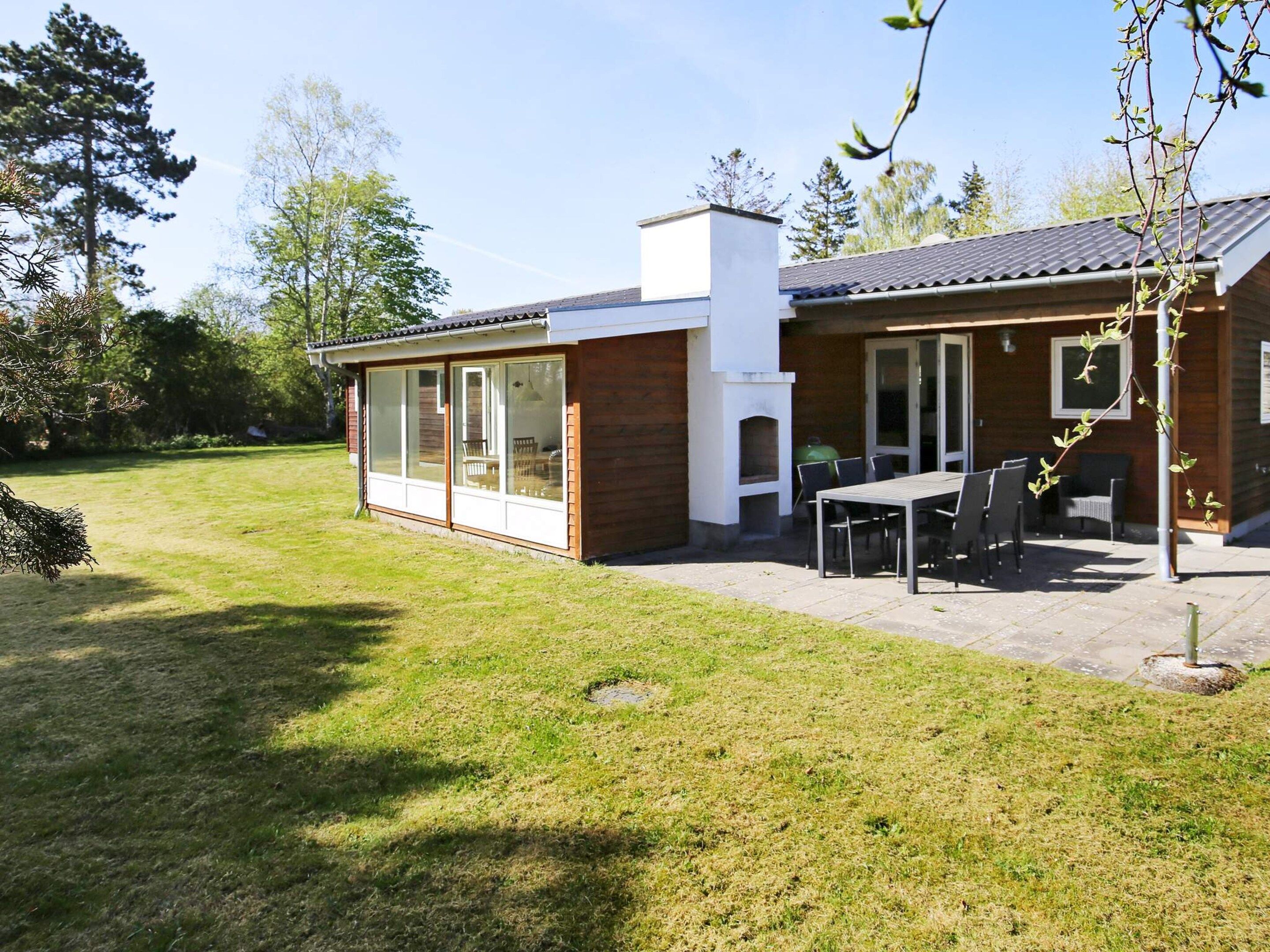 Une maison moderne dotée d’un patio, d’un espace barbecue et d’un ensemble de mobilier de jardin pour les repas.