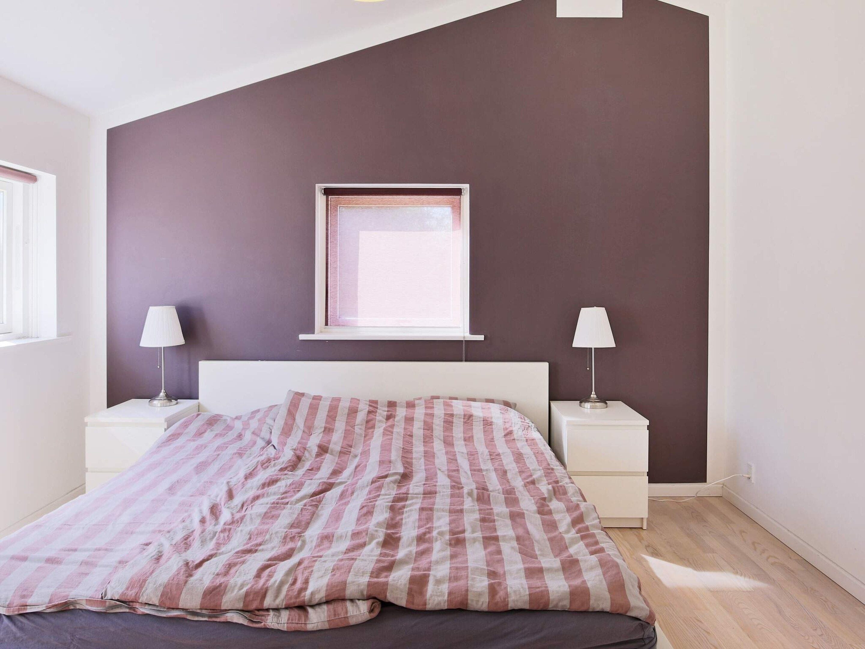 A bedroom with a bed, two bedside tables, a window, and a wall-mounted picture frame.