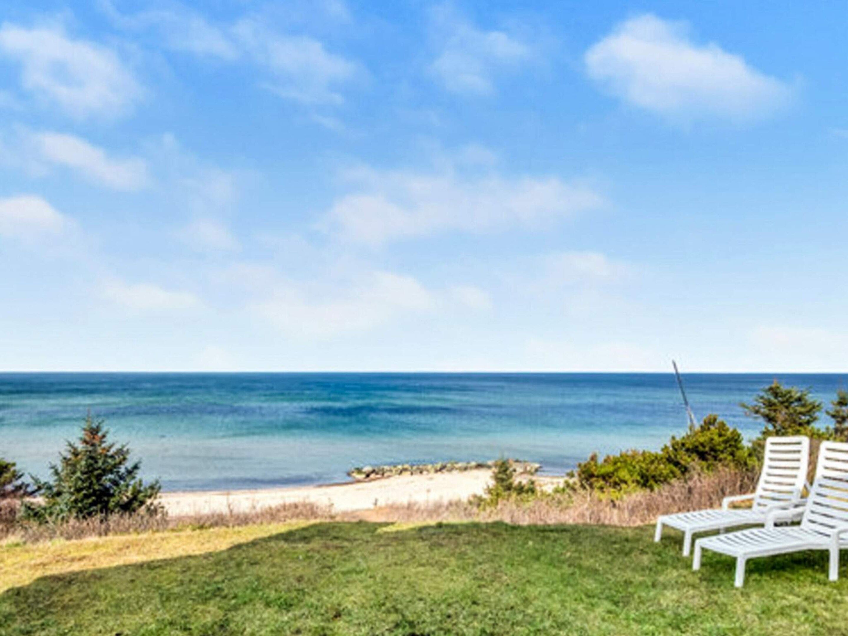 A beach view with two white lounge chairs and a fishing rod.
