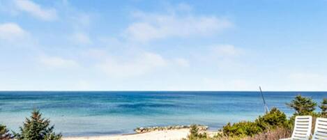 A beach view with two white lounge chairs and a fishing rod.
