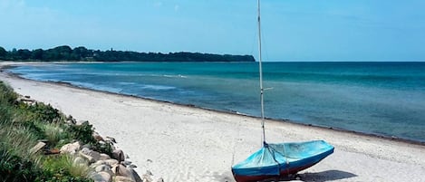Una playa con un velero en la arena, un litoral rocoso y una vista despejada del mar.