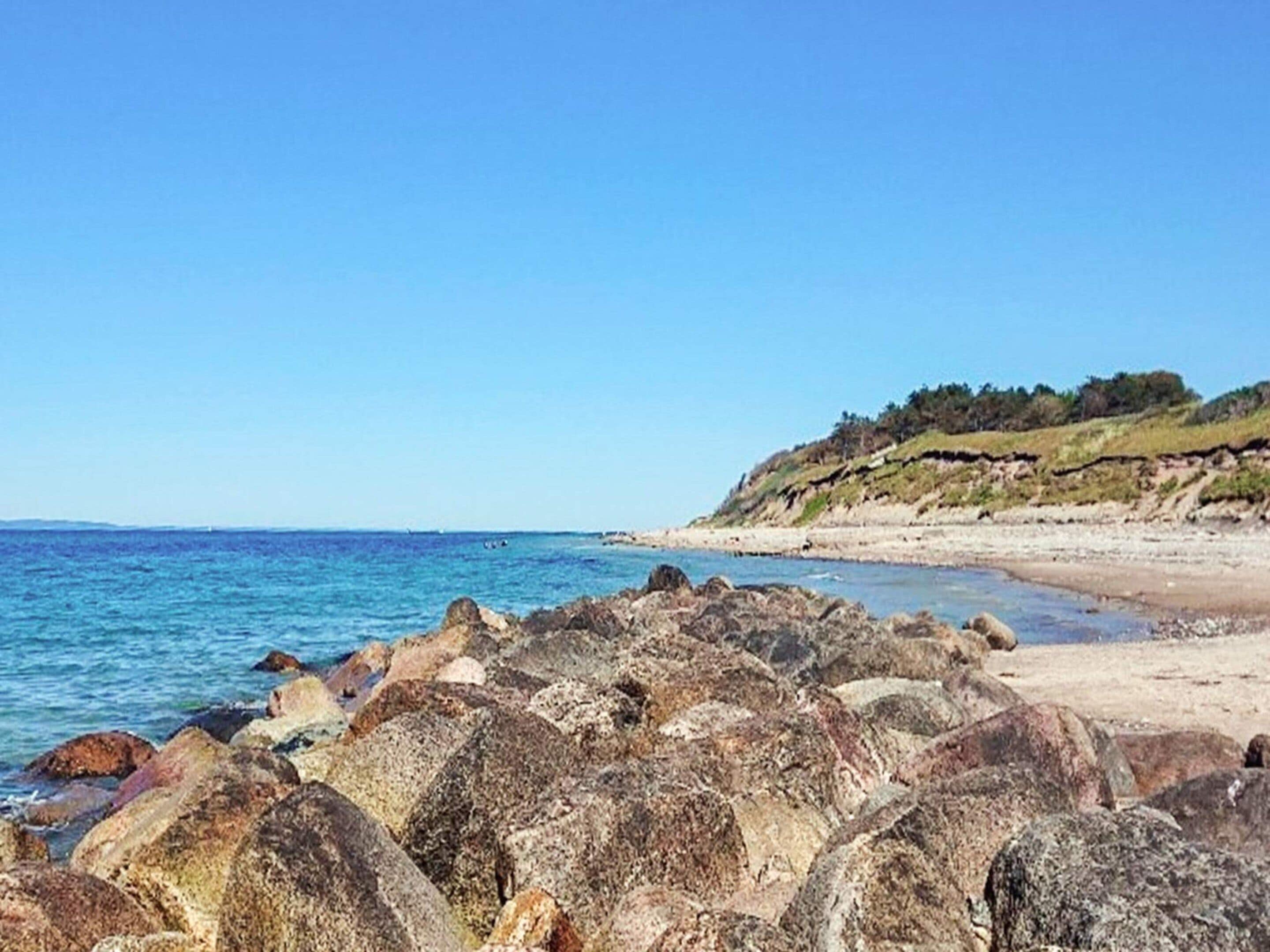 A coastal landscape with rocky outcrops, a sandy beach, and a clear blue sky.