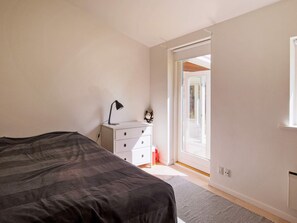 Un dormitorio con una cama, una mesita de noche con lámpara, un aparador y una puerta que da a un espacio al aire libre.