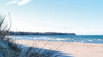 En strand med sand og sparsom vegetation, en klar himmel og en fjer borte kystlinje.