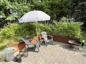 An outdoor patio area with two Adirondack chairs, a round table, and a white umbrella.