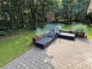A patio with a seating area, surrounded by a garden with various plants and a small circular water feature.