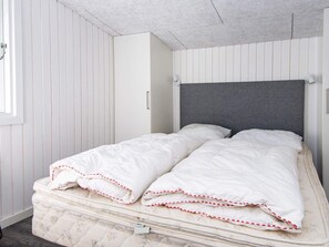 Una cama con cabecera gris, ropa de cama blanca y un colchón con motivos florales.
