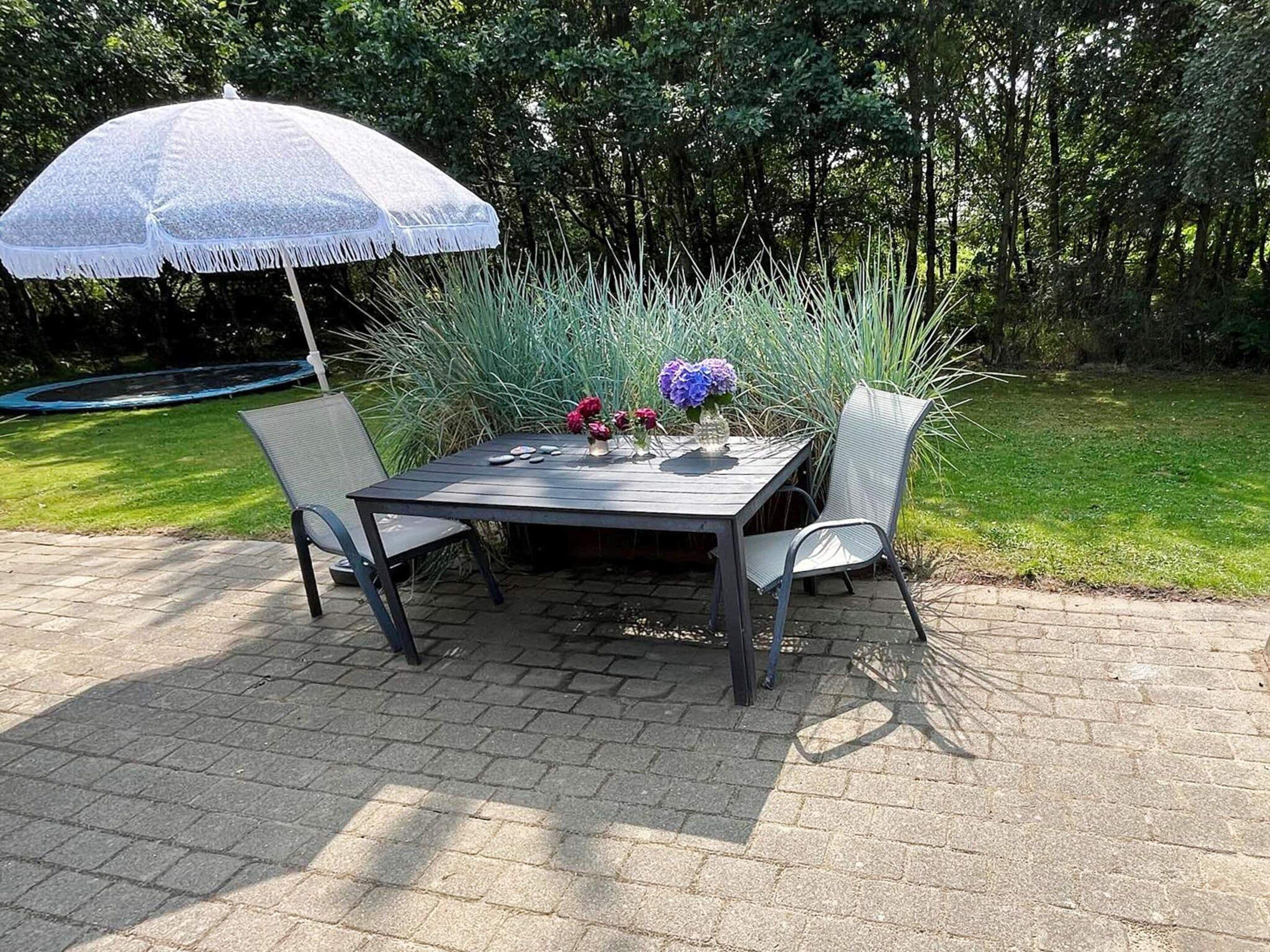 Une terrasse extérieure avec une table, des chaises, un parasol et un arrangement floral.