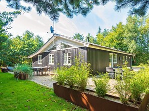 A wooden cabin with a patio, surrounded by greenery.