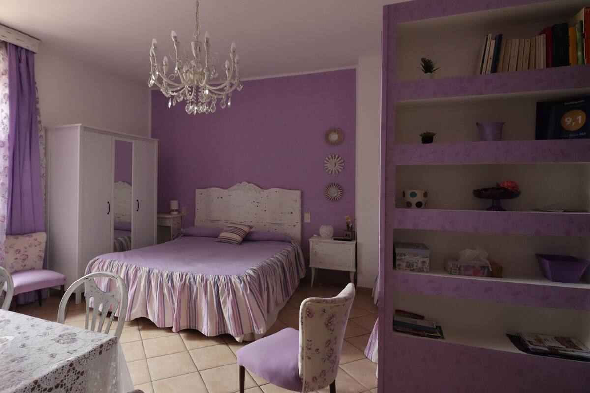 A bedroom with a bed, a chandelier, a wardrobe, a bookshelf, and a chair.