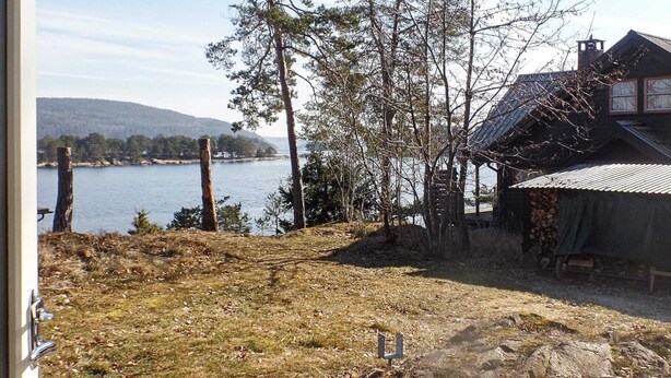 A wooden deck leading to a rustic cabin by a lake with trees and hills in the background. - 7 Person Holiday Home in Aros (Asker)