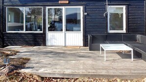 A building with a dark exterior, a white door, and a small porch area with a bench and table. - 7 Person Holiday Home in Aros (Asker)