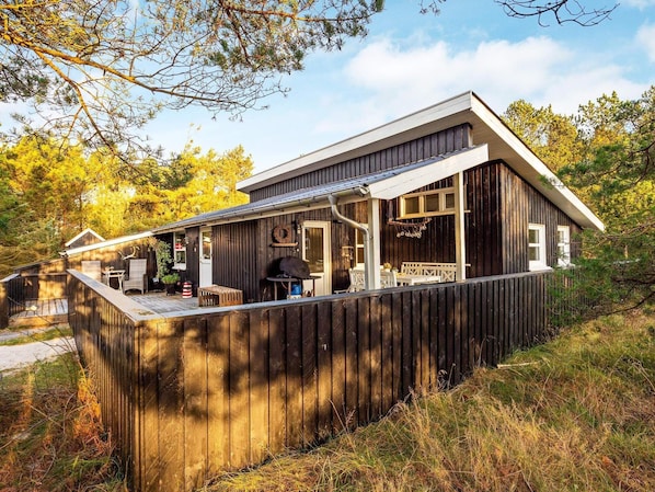 Une cabane en bois dotée d’une véranda, d’un coin repas et d’un petit espace extérieur aménagé pour s’asseoir.