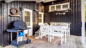 A wooden deck with a barbecue grill, white outdoor furniture, and a hanging light fixture.