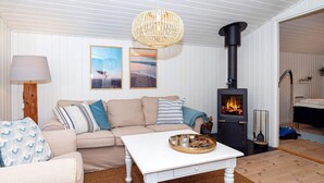 A cozy living room with a beige sofa, a white coffee table, and a wood-burning stove.