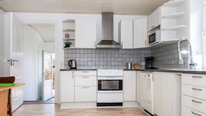 Ett modernt kök med vita skåp, en rostfri köksfläkt, en inbyggd ugn och en diskmaskin.