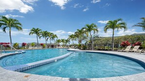 A swimming pool with a curved design, surrounded by palm trees and lounge chairs. - 🌴 Ocean View Townhome | Free Late Checkout 🌴 (Kailua Kona)