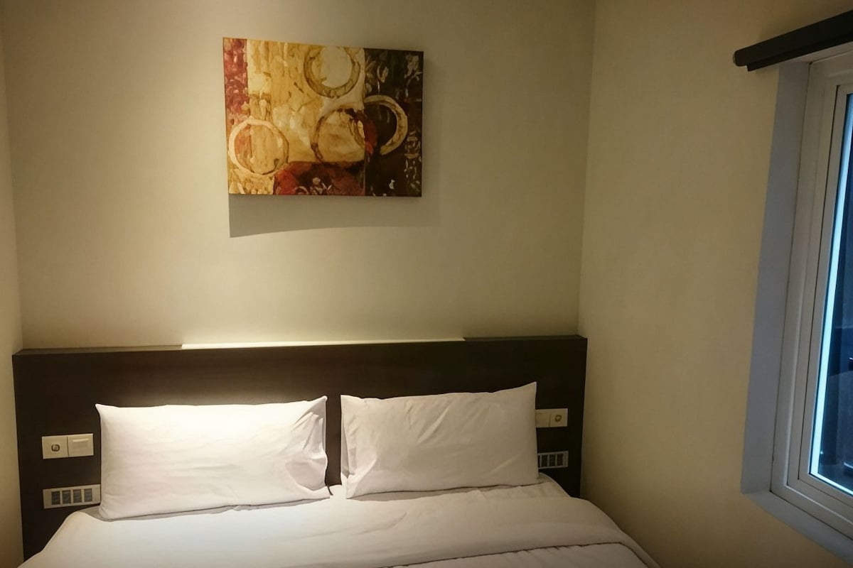 Een hotelkamer met een bed, een hoofdbord, een kunstwerk aan de muur en een raam.