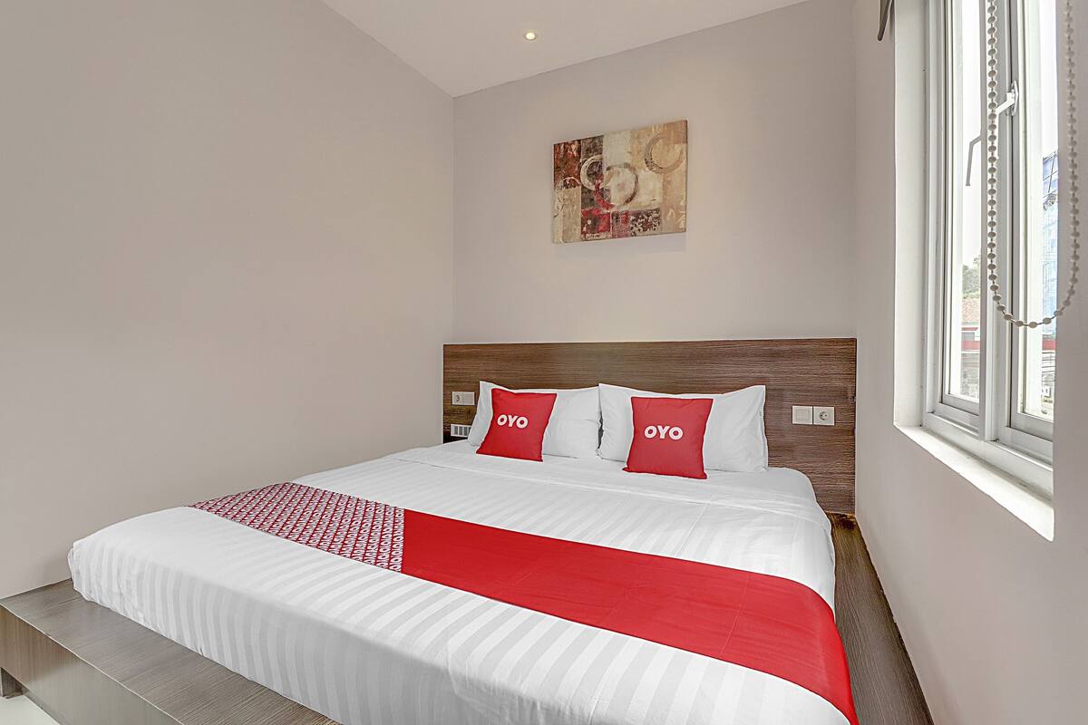 Un lit bien fait, recouvert d’une couvre-lit rouge et blanche, avec deux oreillers sur lesquels est inscrit le mot « OYO », et une tête de lit en bois.