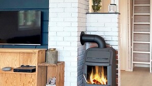 A modern living room with a TV, wooden cabinet, and a black wood-burning stove. - 6 Person Holiday Home in Korssund (Fjaler)