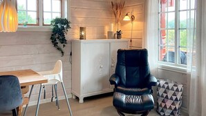 A room with a wooden floor, a white cabinet, a blue leather chair, a wooden table with a white chair, and a window with curtains. - 6 Person Holiday Home in Korssund (Fjaler)
