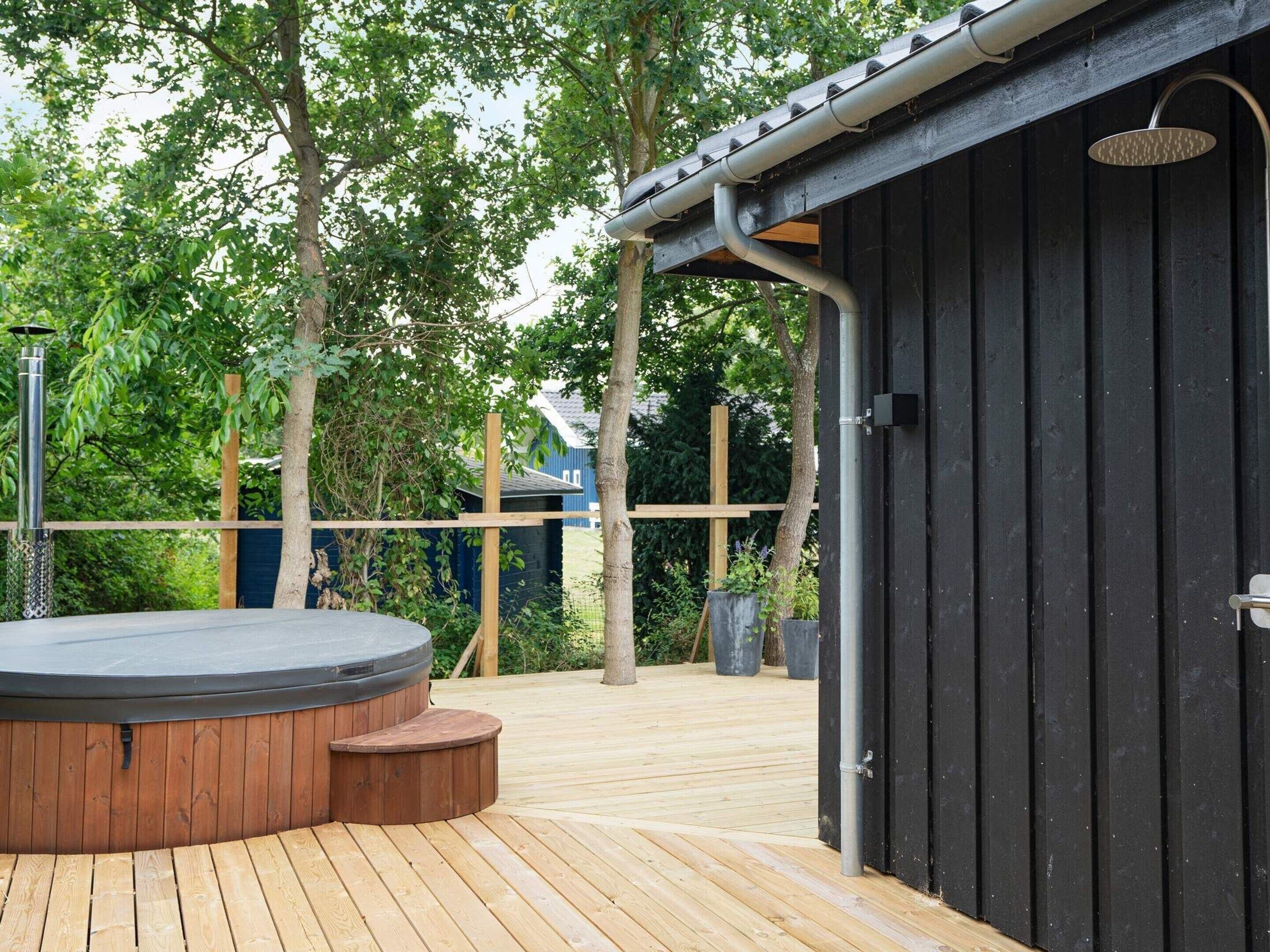 Eine Holzterrasse mit Whirlpool und überdachter Dusche.