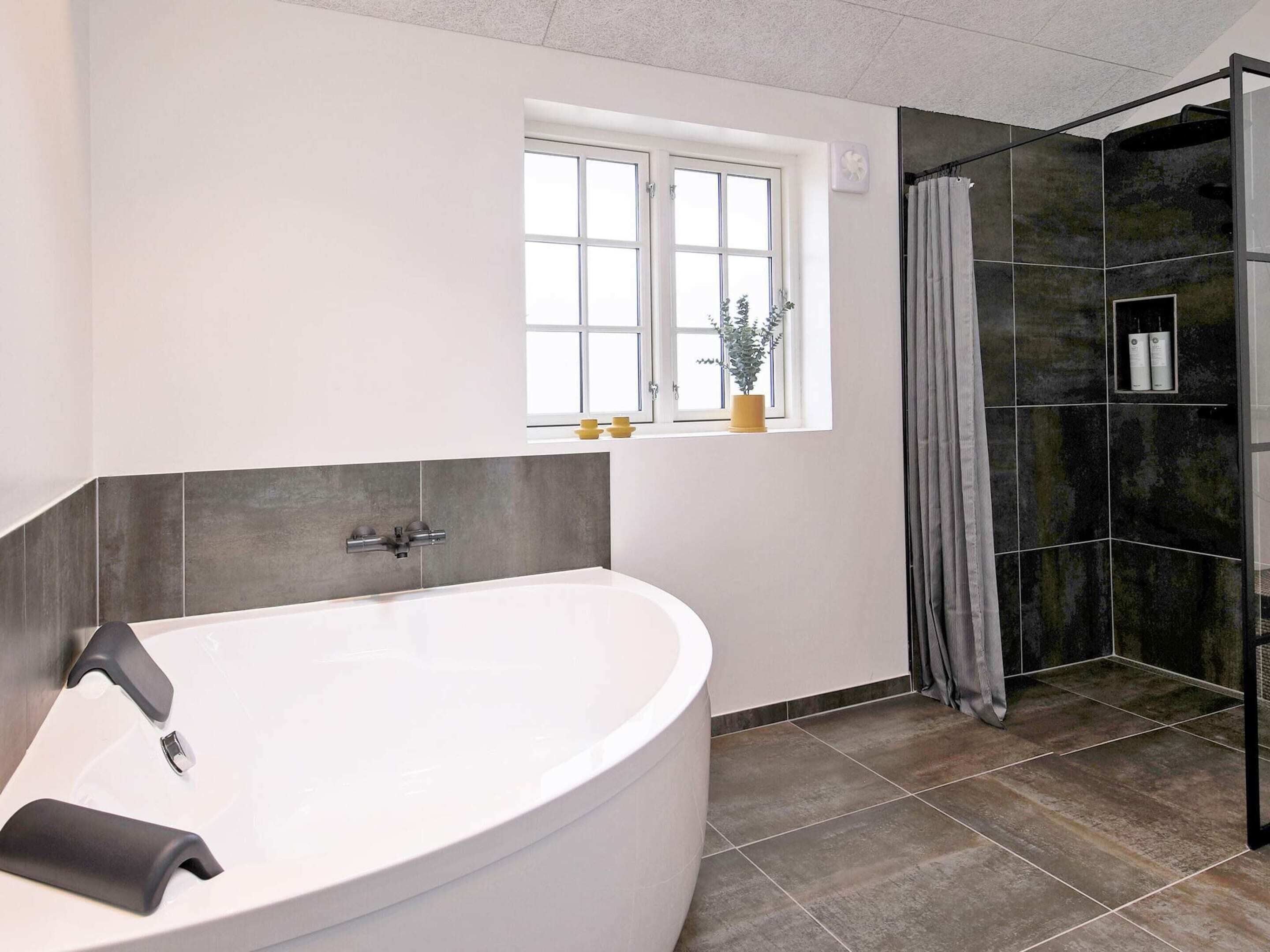 A modern bathroom with a freestanding bathtub, a shower enclosure, and a window with a plant.