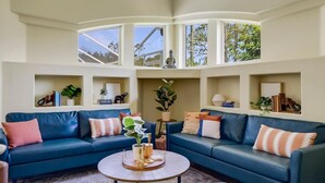 Un salon moderne avec un canapé bleu, une table basse ronde et des étagères intégrées ornées d’objets décoratifs.