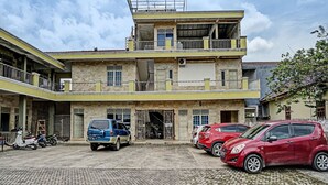 Un immeuble de deux étages avec un balcon à l’étage supérieur, une entrée de garage et plusieurs voitures garées.