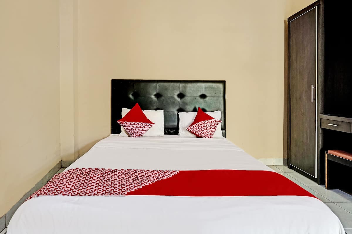 Une chambre d’hôtel avec un lit, une armoire et une couvre-lit à motifs rouges et blancs.