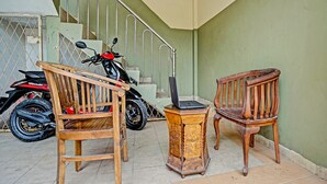 Un escalier avec une rampe en métal, deux chaises en bois, une petite table en bois sur laquelle se trouve un ordinateur portable, et une moto garée à proximité.