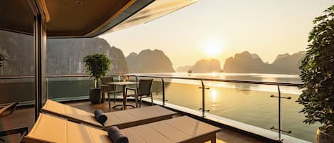 Une terrasse avec une table et des chaises, donnant sur une étendue d’eau calme, avec des montagnes en arrière-plan.