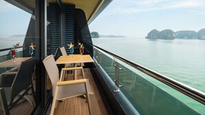 A dining area with a table and chairs, a view of the water, and a wooden ceiling. - Doria Cruise (Tuan Chau)