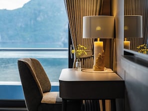 Una habitación con vistas al mar, una mesa con una lámpara, un florero con flores y una vela.