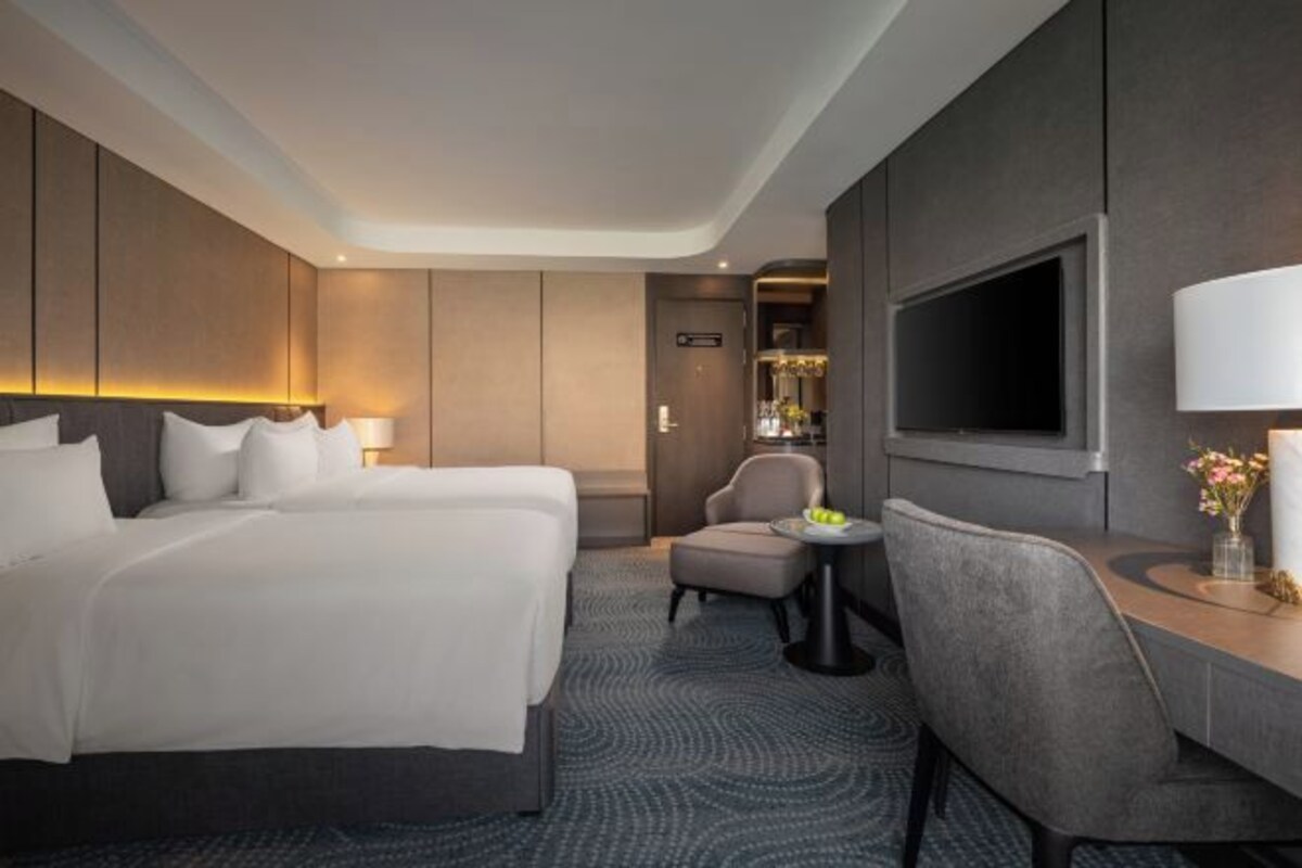 Habitación de hotel con una cama grande, un escritorio, una silla, un televisor y una pequeña mesa con un florero.