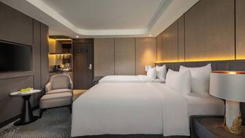 Une chambre d’hôtel avec un grand lit, une chaise, une télévision et une petite table sur laquelle se trouve une assiette de fruits.