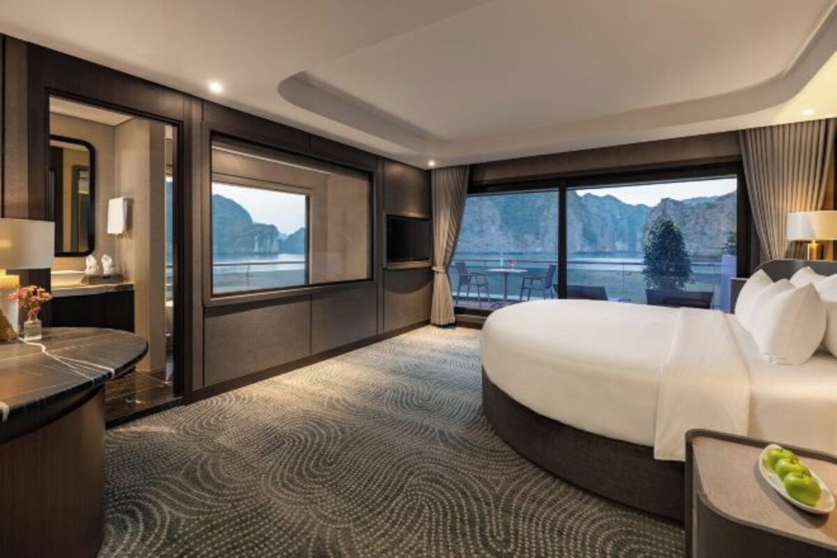 Habitación de hotel con una cama grande, un escritorio, una silla, un televisor, un ventanal con vista a las montañas y un balcón.