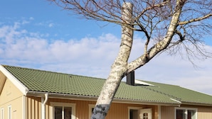 Un edificio a due piani con tetto verde, un pontile in legno e un'area pranzo con sedie.