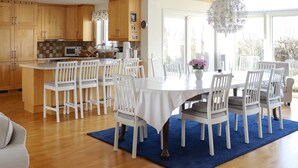 A modern kitchen with wooden cabinets, a central island, and a dining area with white chairs and a table. - 5 Star Holiday Home in Mellbystrand (Mellbystrand)