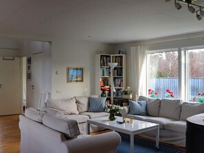 A living room with a sofa set, a coffee table, a bookshelf, and a window with a view of trees.